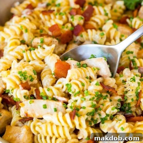 A skillet of chicken bacon ranch pasta with a serving spoon in it.