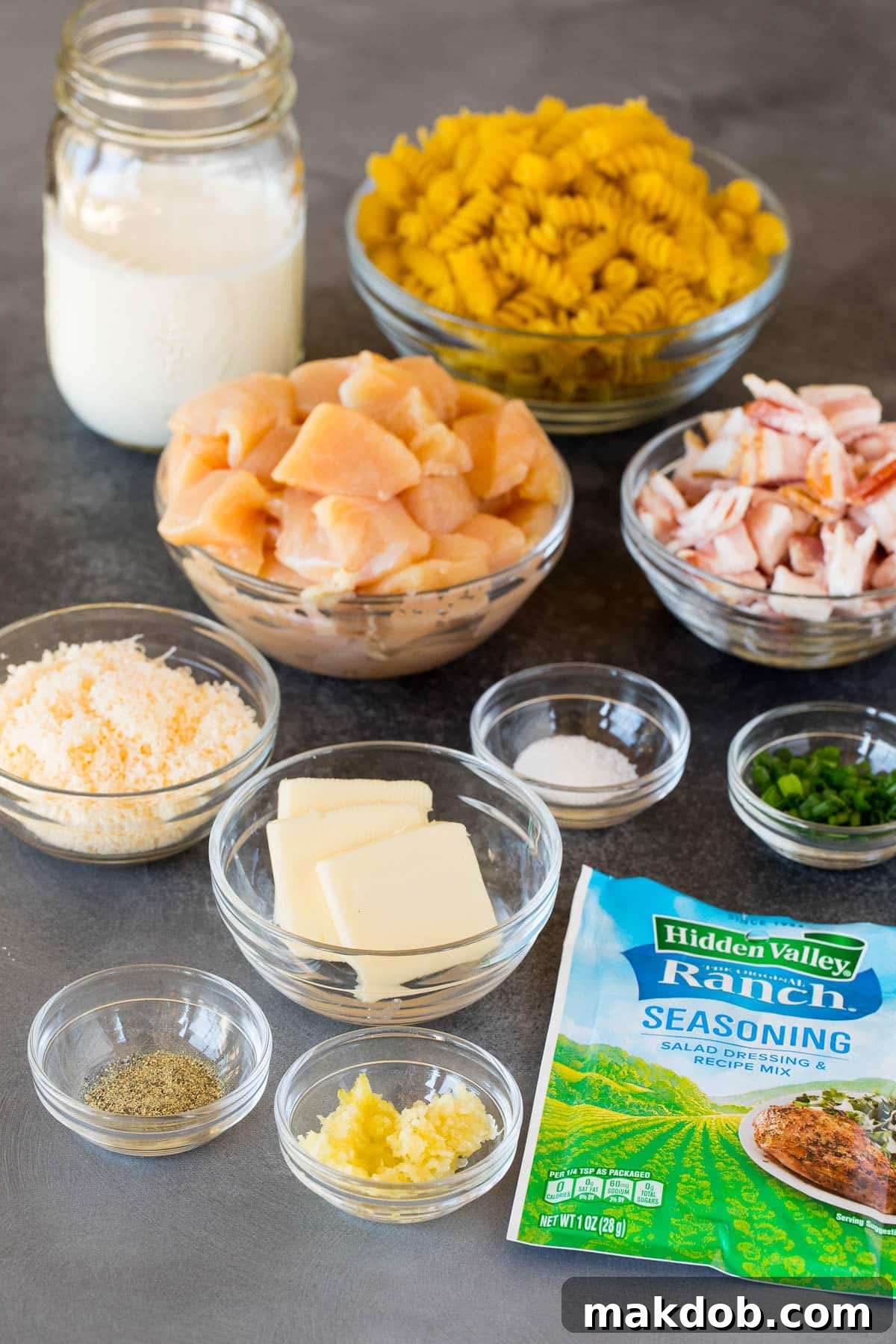 Bowls of ingredients including uncooked rotini pasta, butter, fresh herbs, grated Parmesan cheese, and ranch seasoning.
