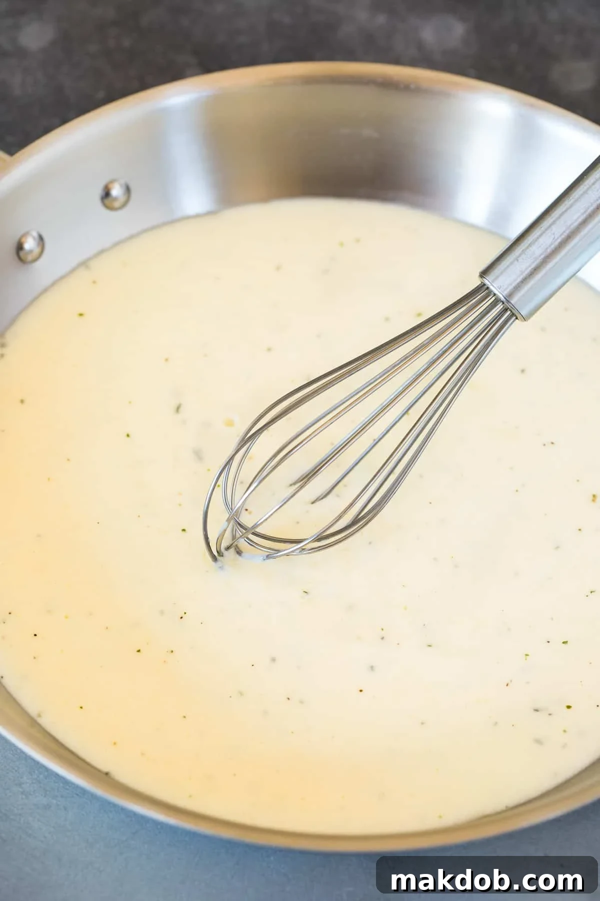 A pan of creamy white sauce with a whisk in it, showcasing the rich texture before pasta is added.