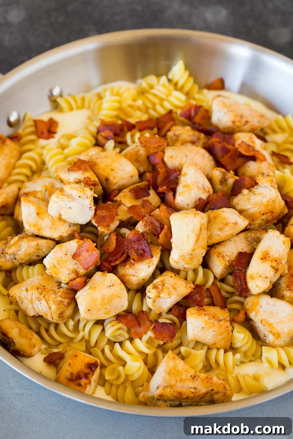 Chicken, rotini pasta, and crispy bacon mixed in a pan of creamy sauce, ready for serving.