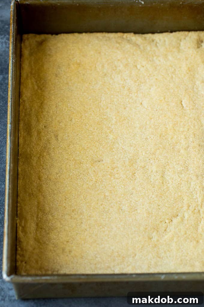 A golden brown shortbread crust baking in a square pan, ready for its pecan filling.
