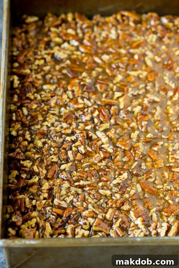 Gooey pecan filling poured over a baked shortbread crust in a pan, before final baking.