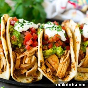A plate of perfectly prepared slow cooker chicken tacos, generously topped with creamy guacamole, fresh pico de gallo, and a dollop of sour cream.