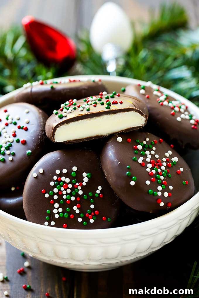A bowl of freshly made homemade peppermint patties, some cut in half to show the creamy mint center.