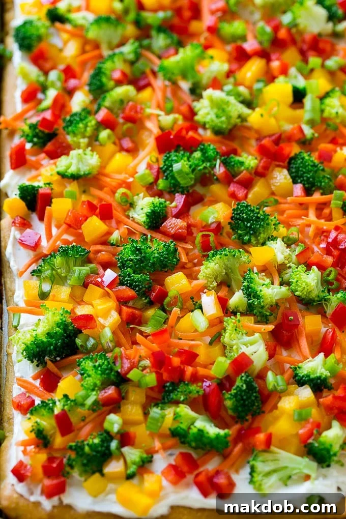 A beautifully arranged veggie pizza on a crispy crescent roll crust, topped with ranch cream cheese and an assortment of colorful, fresh vegetables, ready to be served at a party or family gathering.
