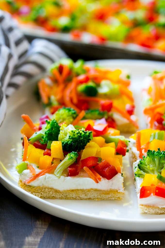 Slices of the fresh and colorful veggie pizza arranged on a serving plate, highlighting the crisp vegetables and creamy ranch layer on a golden crescent roll crust.