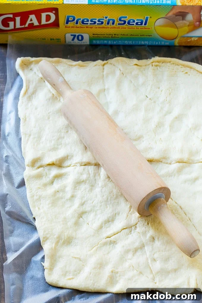 Crescent roll dough carefully unrolled and pressed into an even rectangle on a baking sheet, ready for baking to form the crispy base of the veggie pizza.