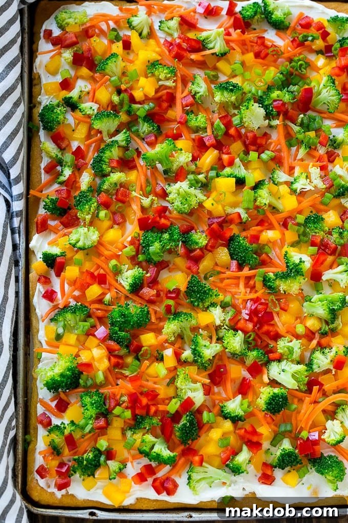 A sheet pan filled with a freshly assembled crescent roll veggie pizza, showcasing the vibrant colors of the vegetables and the creamy ranch base before chilling.