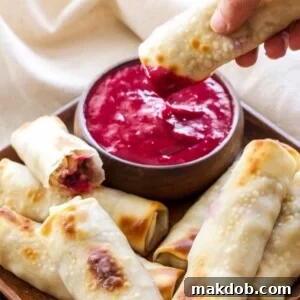 A picture of turkey, cranberry and brie eggrolls on a plate with one being dipped in sauce.