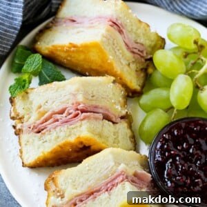 A plated Monte Cristo Sandwich accompanied by fresh fruit and a side of vibrant raspberry jam for dipping.