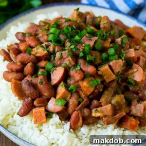 A vibrant plate of Red Beans and Rice, generously topped with savory sausage, tender ham, and fresh herbs.