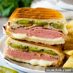 A perfectly pressed Cuban Sandwich, revealing delicious layers of ham, roasted pork, Swiss cheese, and tangy pickles.