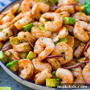 A serving bowl of Mexican shrimp cocktail which contains small shrimp, diced avocado, herbs and jalapeno.