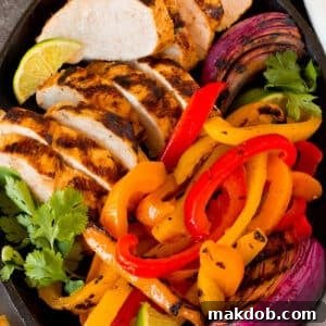 A platter of grilled chicken fajitas with onions, bell peppers, lime wedges and fresh cilantro.