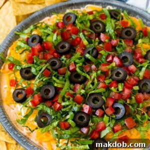 Taco dip with layers of seasoned cream cheese, lettuce, tomato, shredded cheese and olives.