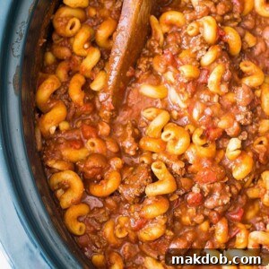 A comforting image of chili mac simmering in a slow cooker, with a wooden spoon scooping out a generous portion.