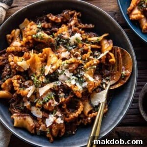 A picture of slow cooker red wine braised short rib pasta in a blue bowl with a fork and spoon.