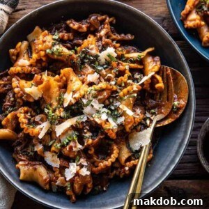 A picture of slow cooker red wine braised short rib pasta served in a blue bowl with a fork and spoon, highlighting the rich sauce and tender beef.