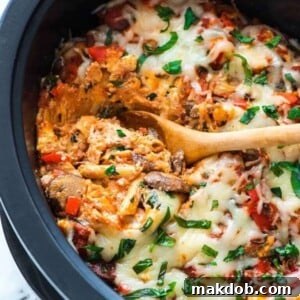 An appetizing image of creamy crock pot pasta in a slow cooker, with a wooden spoon nestled within, inviting you to dig in.