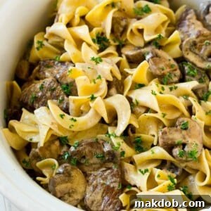 Slow cooker beef stroganoff with chunks of beef, mushrooms and egg noodles topped with parsley.