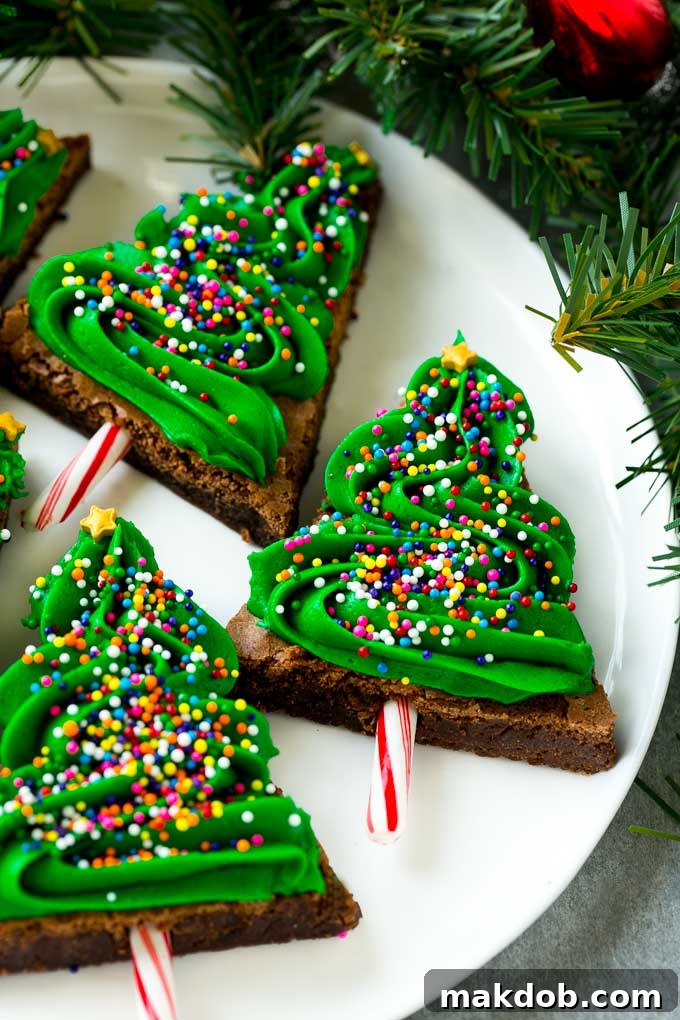 Yuletide Fudge Trees 3 A delectable plate of Christmas tree brownies, lavishly topped with vibrant green frosting and an abundance of rainbow sprinkles.