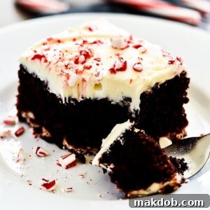 A slice of Chocolate Candy Cane Cheesecake Cake, showcasing elegant swirls of cheesecake, rich chocolate cake, and a beautiful cream cheese frosting topped with crushed candy canes.