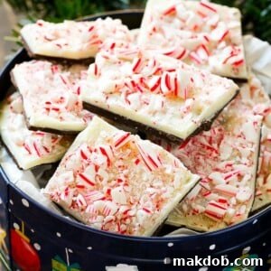 Generous pieces of classic Peppermint Bark, showcasing layers of white and dark chocolate topped with vibrant crushed candy canes, nestled in a festive holiday tin.