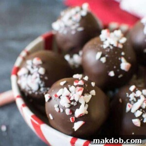 A bowl filled with smooth Candy Cane Sugar Cookie Truffles, delicately coated in chocolate and sprinkled with crushed candy canes for a festive touch.