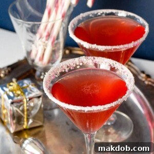 Two elegant Candy Cane Cocktails served on a silver tray, adorned with festive candy cane rims and a hint of homemade infused vodka for a sophisticated holiday drink.