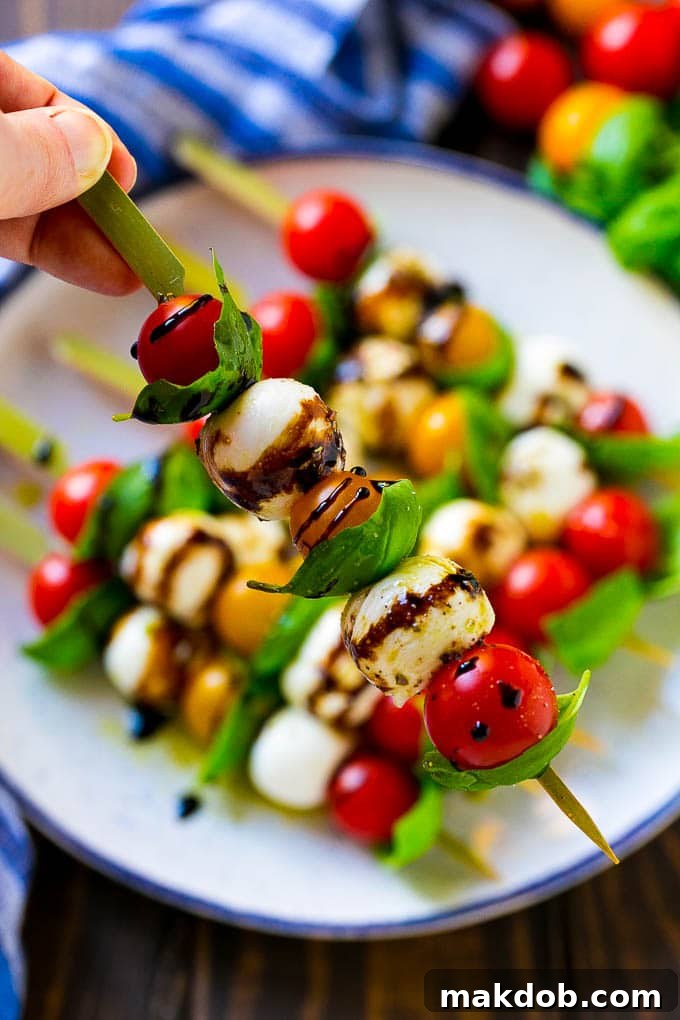 A beautifully presented Caprese kabob, featuring layers of fresh mozzarella, ripe cherry tomatoes, and aromatic basil leaves, all glistening with a balsamic glaze drizzle.