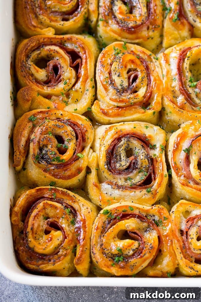 Ham and Cheese Pinwheels Recipe | Ham and Cheese Roll Ups | Ham and Cheese Rolls | Ham and Cheese Bread Rolls Golden brown Ham and Cheese Pinwheels in a baking dish, garnished with fresh parsley.