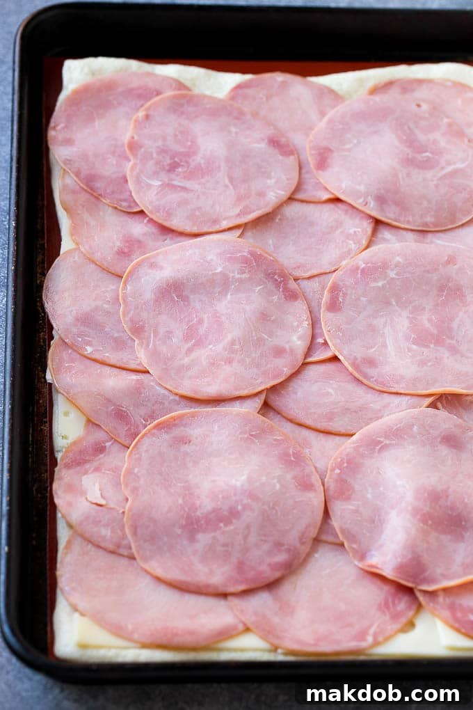 Ham and Cheese Pinwheels Recipe Preparation Slices of ham and Swiss cheese layered neatly on pizza dough before rolling.
