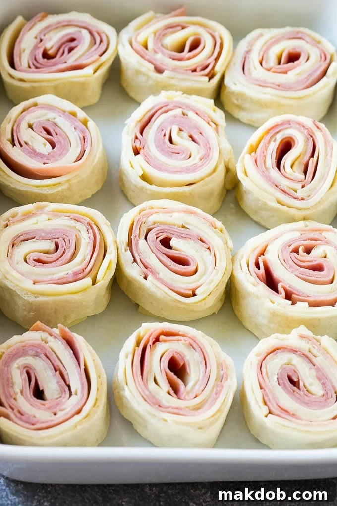Ham and Cheese Pinwheels Ready to Bake Rolled up ham, cheese, and pizza dough circles arranged in a baking dish, ready for the oven.