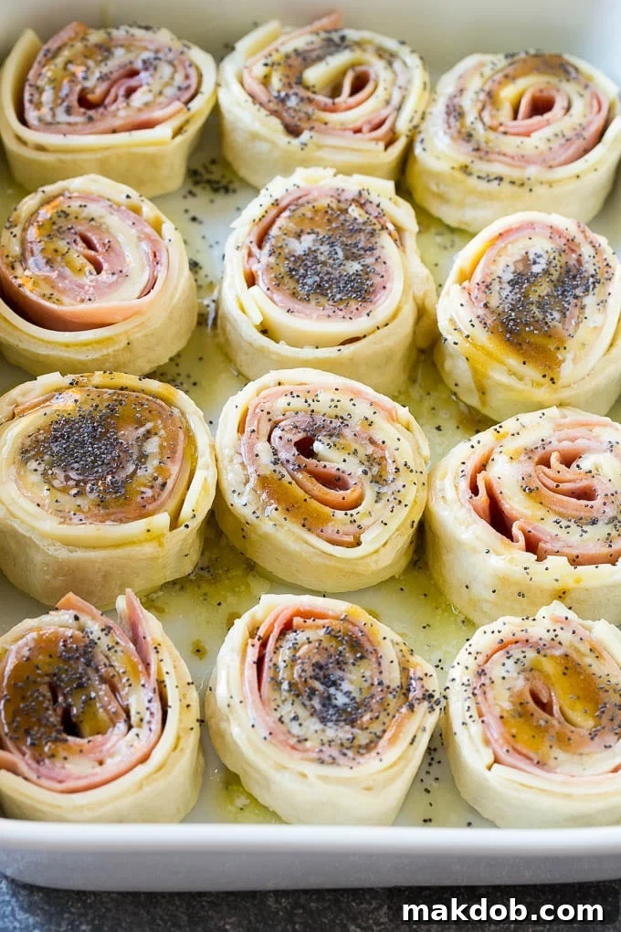 Hot Ham and Cheese Pinwheels with Poppy Seed Glaze Baked ham and cheese pinwheels topped with a glistening poppy seed butter sauce in a ceramic baking dish.