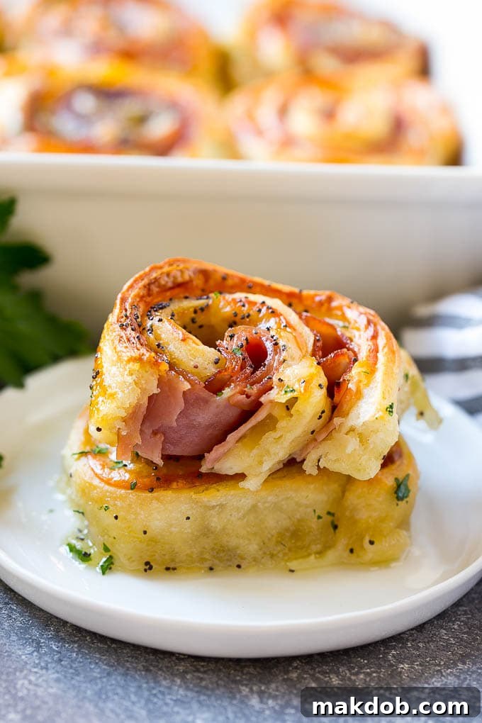 Served Ham and Cheese Pinwheels Appetizer Stack of golden brown ham and cheese pinwheels on a white serving plate, garnished with parsley.