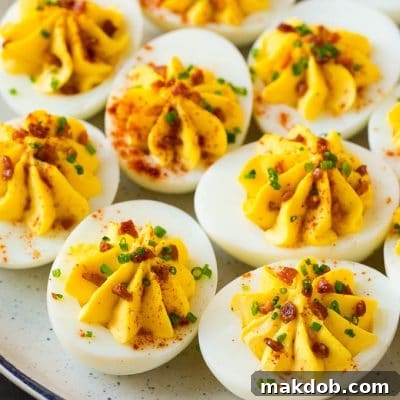 A plate of bacon deviled eggs garnished with sliced chives and smoked paprika.