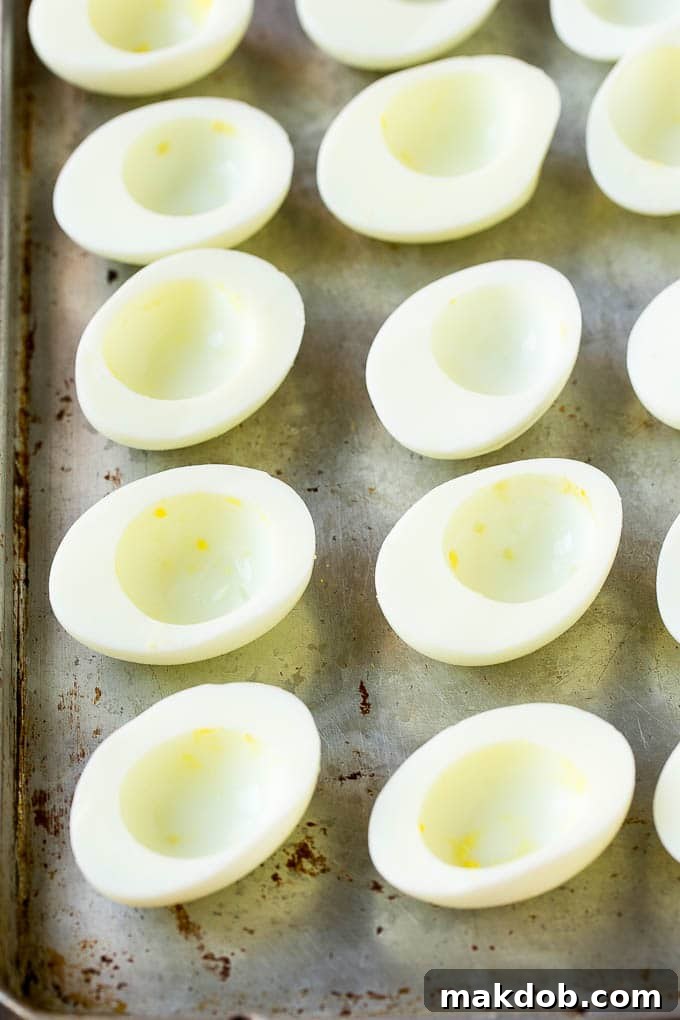 Halved hard-boiled egg whites neatly arranged on a baking sheet, ready for filling. The clean cuts demonstrate successful peeling.