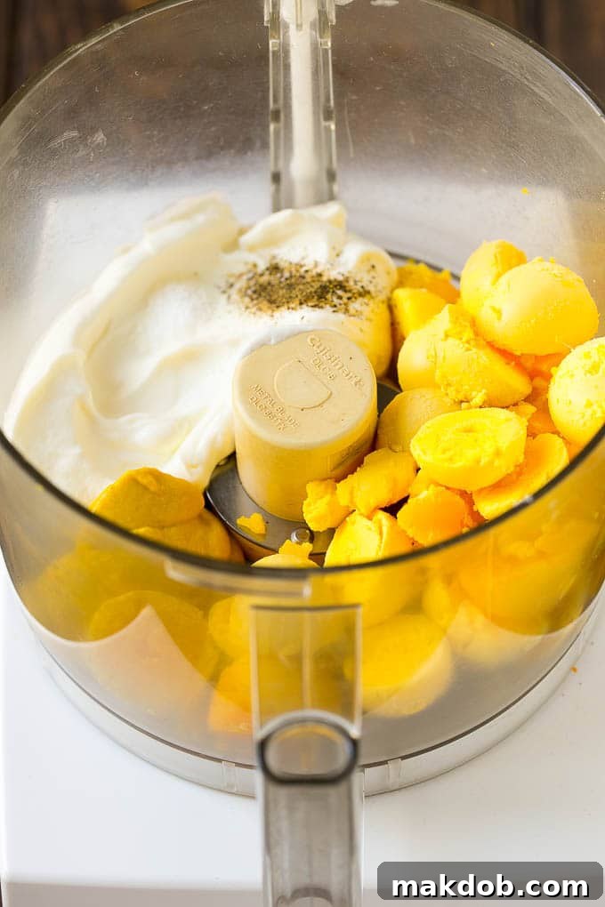 A food processor bowl containing creamy egg yolks, mayonnaise, and seasonings, ready to be blended into a smooth filling for deviled eggs.