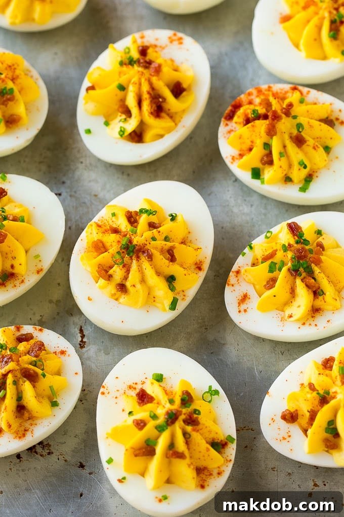 A close-up of bacon deviled eggs arranged on a platter, meticulously topped with crispy bacon bits, fresh chives, and a light dusting of smoked paprika, highlighting their appetizing appeal.