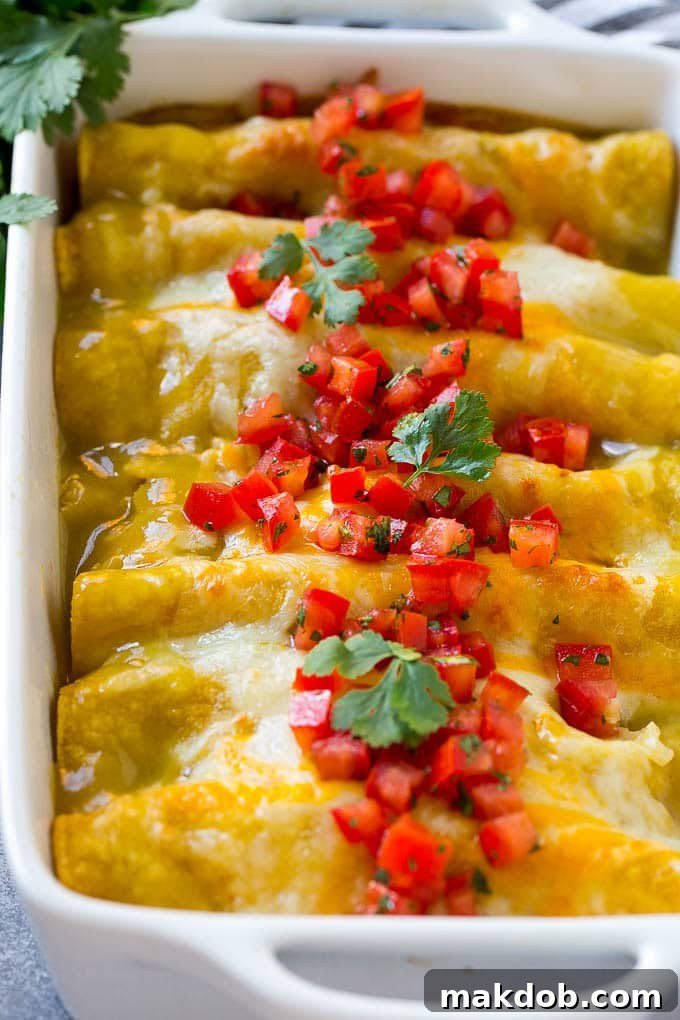 A pan full of green chile chicken enchiladas topped with diced tomatoes and cilantro.
