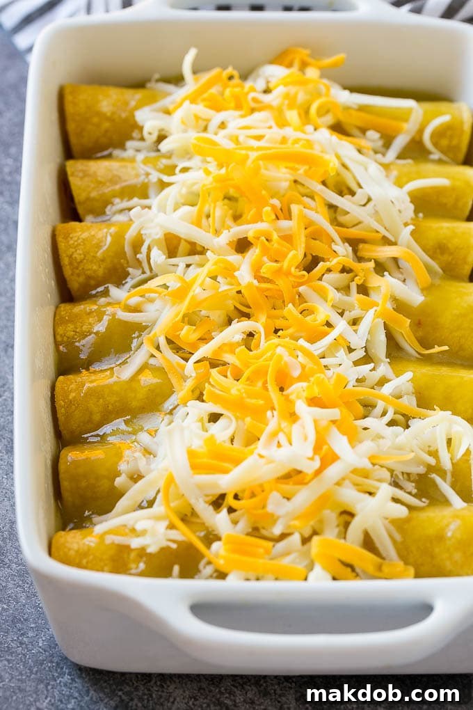 Unbaked green chile chicken enchiladas topped with shredded cheese.