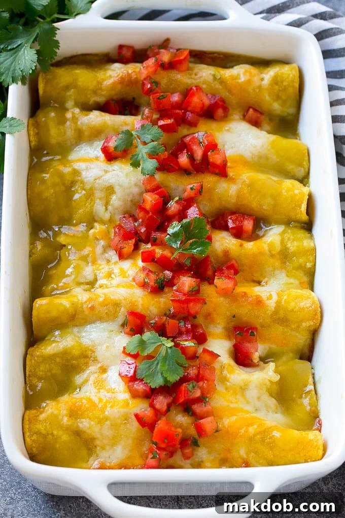 A baking dish of green chile chicken enchiladas topped with cheese, tomatoes and cilantro leaves.