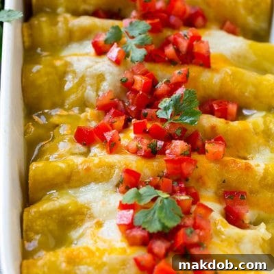 A pan full of green chile chicken enchiladas topped with diced tomatoes and cilantro.