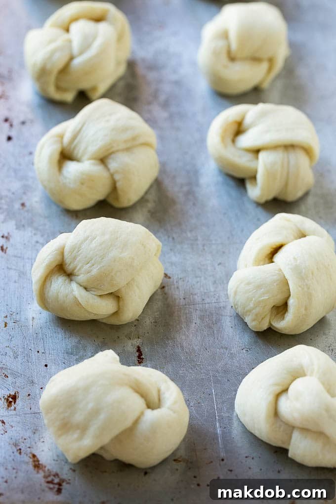 Pizza dough strips expertly tied into neat knots and arranged on a sheet pan, ready for their buttery coating and baking.