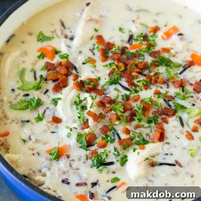 A pot of creamy chicken and wild rice soup with vegetables and bacon.
