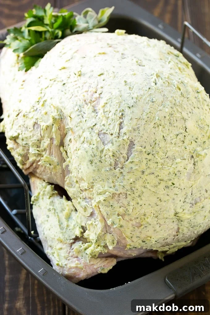 An herb roasted turkey generously coated in the aromatic herb butter, showcasing its readiness for roasting and promising a delicious, crispy skin.