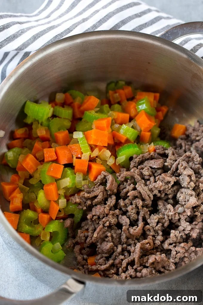 Loaded Burger Soup 4 Ground beef being added to the sautéed vegetables in a large pot, ready to be browned for hamburger soup.