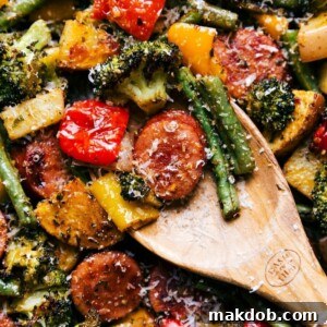 An image of a wooden spoon showcasing roasted veggies and perfectly sliced sausage pieces.