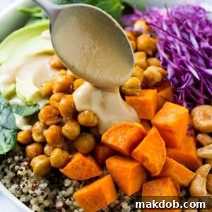 A colorful Buddha Bowl featuring quinoa, chickpeas, sweet potatoes, avocado, cabbage, and a drizzle of tahini dressing.