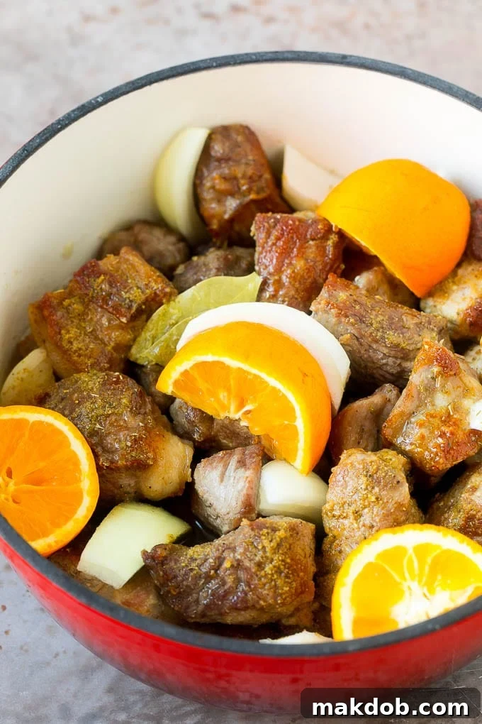 Pork shoulder pieces, oranges and onion in a pot.